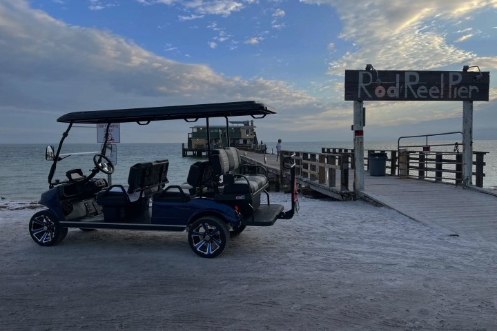 Golf cart parked near Rod and Reel Pier with ocean in background under a partly cloudy sky.