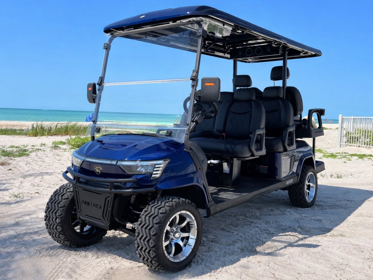 Blue golf cart with black seats on a sandy beach with ocean and blue sky in background.
