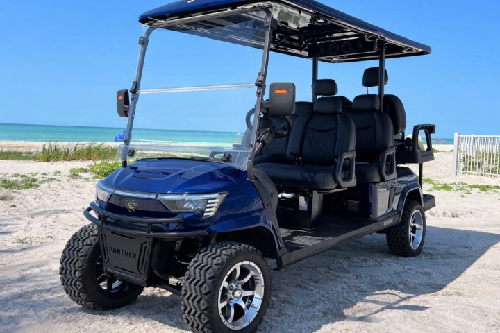 Blue golf cart with black seats on a sandy beach with ocean and blue sky in background.
