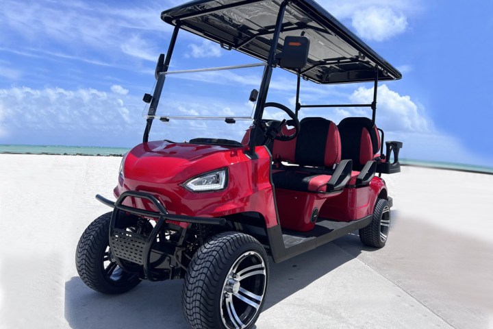 Red golf cart with black roof parked on a sunny beachside path.
