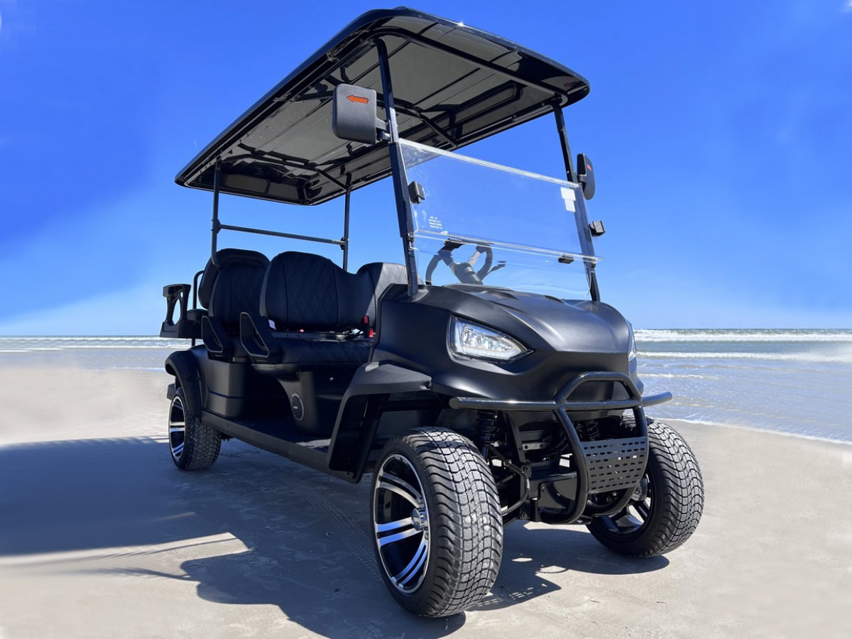 Black golf cart on a sandy beach under a clear blue sky.
