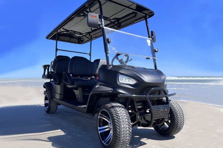 Black golf cart on a sandy beach under a clear blue sky.